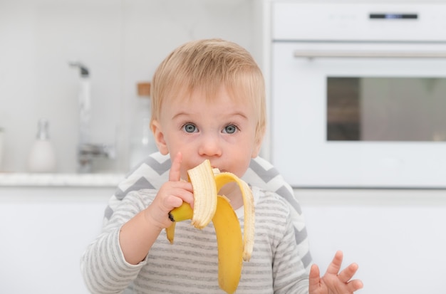 Hermoso niño rubio caucásico de un año de edad sentado en una silla almorzando en la cocina ...