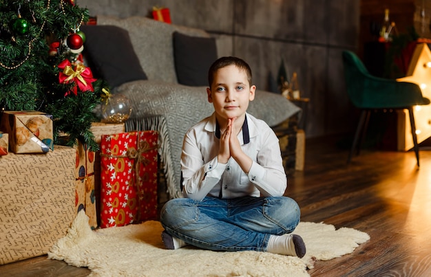 Hermoso niño sentado en el piso junto al árbol de Navidad. Vacaciones en familia