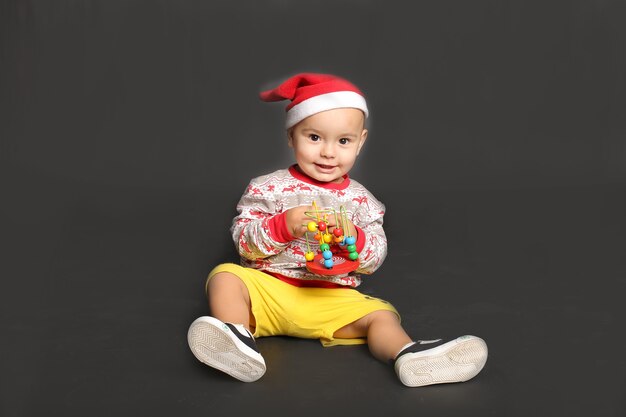 Foto un hermoso niño con un suéter navideño, gorro de papá noel, juega con un juguete