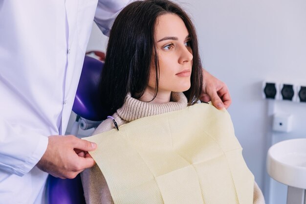 Hermoso paciente en una silla dental con una servilleta visita al