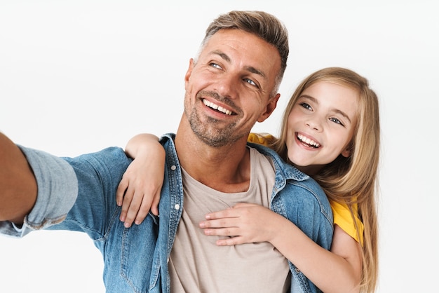 Hermoso padre caucásico que lleva a cuestas a su pequeña hija mientras toma una foto selfie juntos aislado en blanco