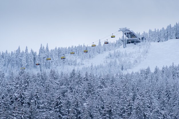 Hermoso paisaje de bosque de montaña de invierno con gente levantando en un telesilla