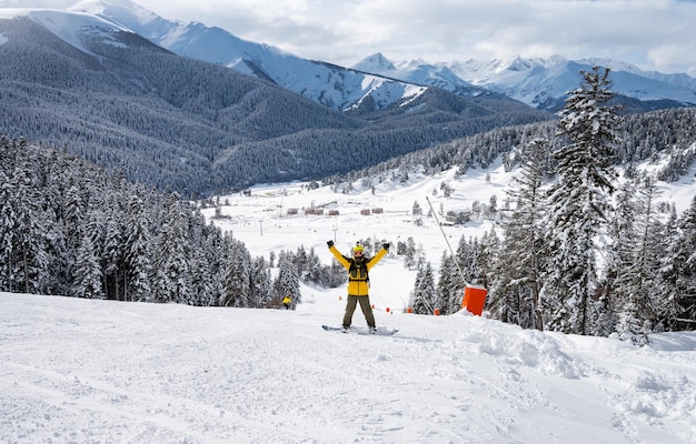 Hermoso paisaje de la estación de esquí de Arkhyz con montañas nevadas y hombre snowboarder con chaqueta amarilla y mochila en un soleado día de invierno Montañas del Cáucaso Rusia