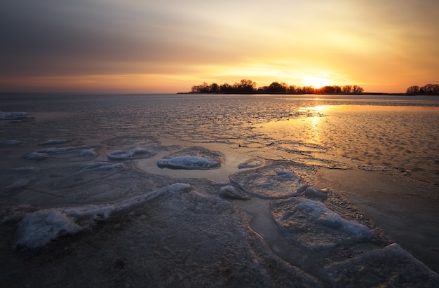 Hermoso paisaje invernal con cielo ardiente al atardecer y lago congelado. Composición de la naturaleza.