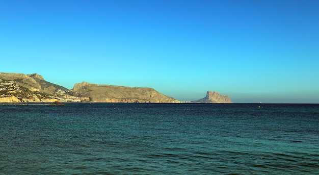 Hermoso paisaje marino, mar azul claro, playa de guijarros, montañas en la distancia, España mediterránea,