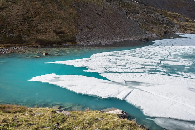 Hermoso paisaje de montaña con lago alpino congelado y piedras en agua transparente El hielo claro flota en la superficie del agua del lago de montaña Impresionante paisaje con lago de montaña helado Fondo de lago de hielo