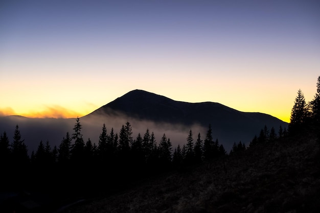 Hermoso paisaje de montaña con picos brumosos y valle brumoso al atardecer.