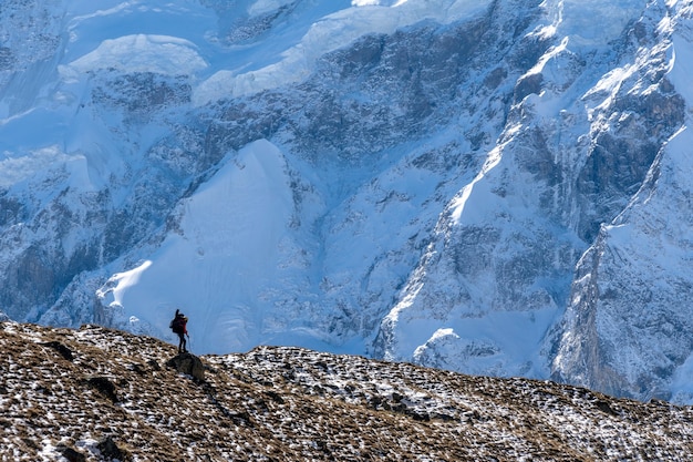 Hermoso paisaje con montañas, glaciar enorme azul y silueta de un hombre caminando con una mochila grande y guitarra en el fondo de montañas y glaciares