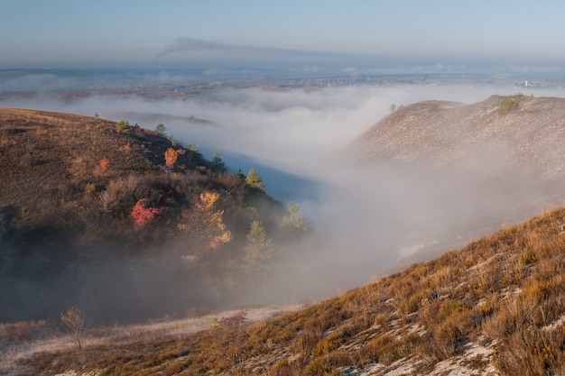 Hermoso paisaje otoñal con río y bosque brumoso en el valle, colinas calcáreas en la niebla