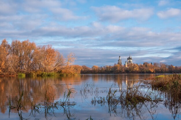 Hermoso paisaje otoñal a la vista de la Iglesia Ortodoxa en la orilla del río. El pueblo de Dedinovo, región de Moscú