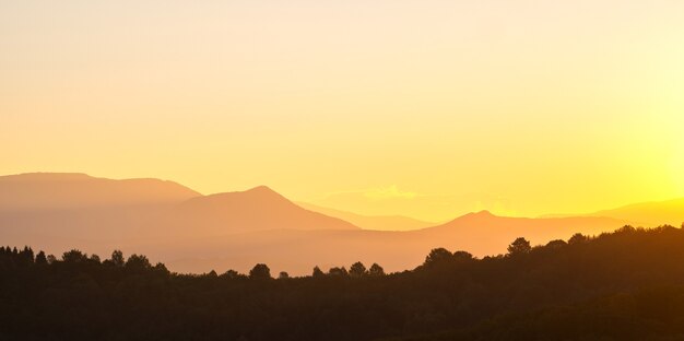 Hermoso paisaje panorámico de montaña con picos brumosos y valle brumoso al atardecer.