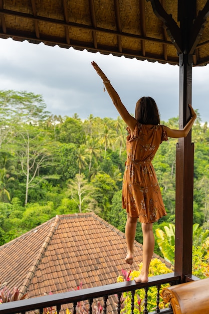 Hermoso paisaje tropical. Bonita chica morena de pie sobre el soporte de madera, mirando hacia la selva tropical