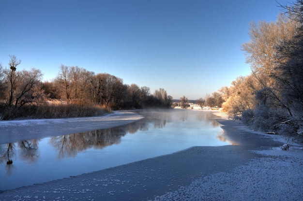 Hermoso panorama de un bosque nevado y un lago de deshielo en un cálido día soleado de primavera