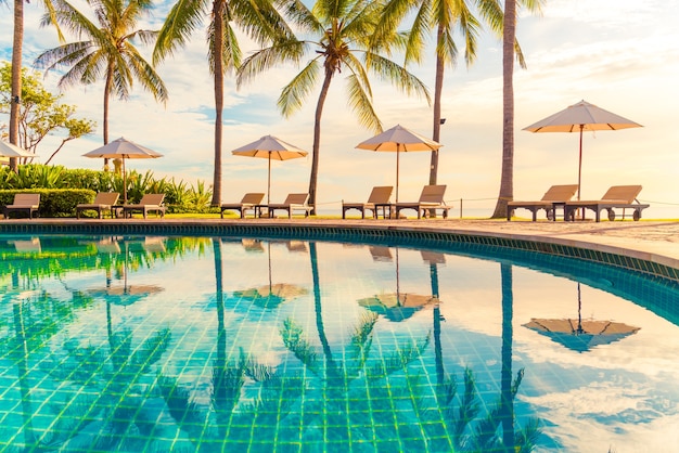 Hermoso paraguas de lujo y una silla alrededor de la piscina al aire libre en el hotel y resort con palmera de coco en el cielo al atardecer o al amanecer. concepto de vacaciones y vacaciones