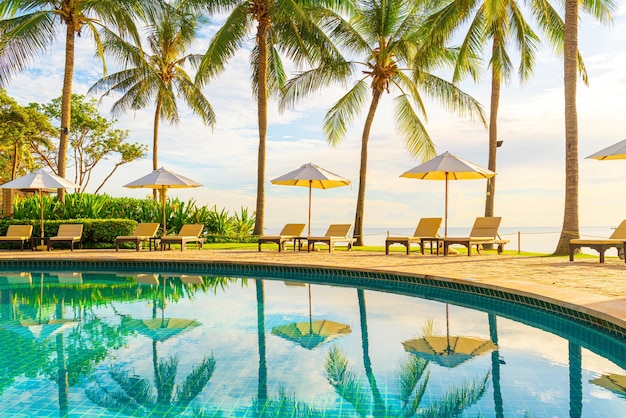 Hermoso paraguas de lujo y una silla alrededor de la piscina al aire libre en el hotel y resort con palmera de coco en el cielo al atardecer o al amanecer - concepto de vacaciones y vacaciones