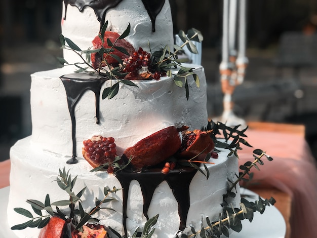 Hermoso pastel de bodas blanco crema de tres niveles con fruta de granada y flores frescas