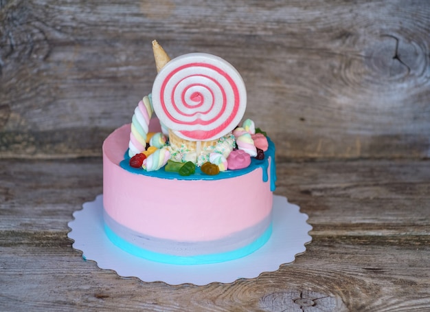 Hermoso pastel casero con crema rosa para el cumpleaños de un niño, decorado con un caramelo grande, malvavisco de cono de waffle, figura de gatito en una mesa de madera