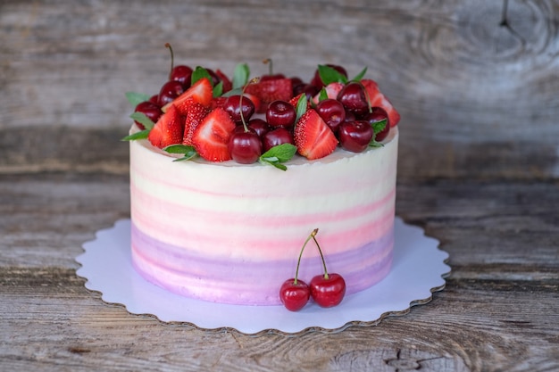 Hermoso pastel casero con delicada crema de color púrpura, rosa y blanco y bayas de fresa y cereza en una mesa de madera