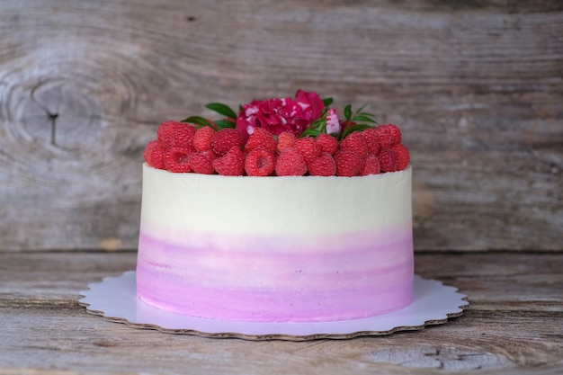 Hermoso pastel casero festivo con crema blanca y morada, decorado con bayas de frambuesa y rosa roja viva