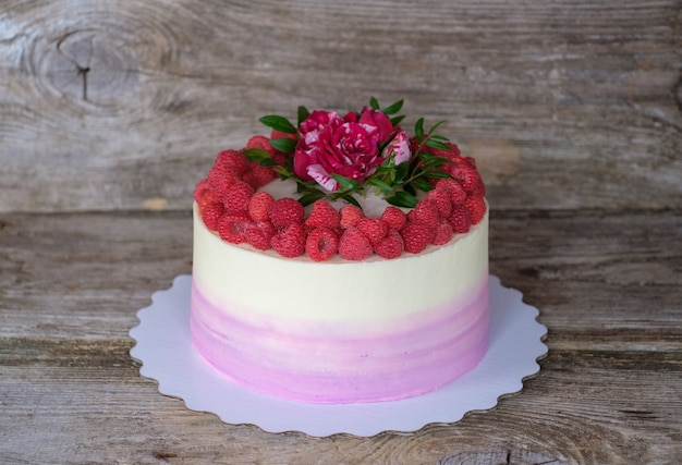 Hermoso pastel casero festivo con crema blanca y morada, decorado con bayas de frambuesa y rosa roja viva