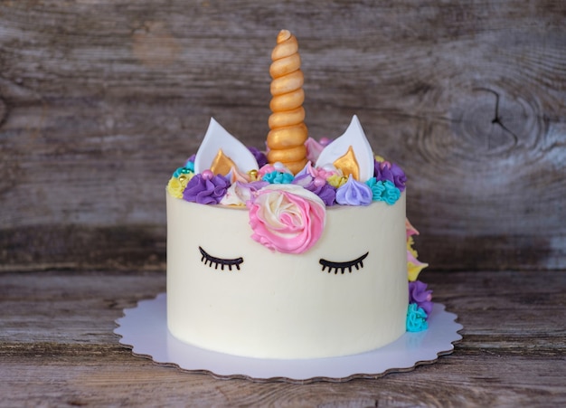 Hermoso pastel casero en forma de unicornio con flores de color crema sobre una mesa de madera