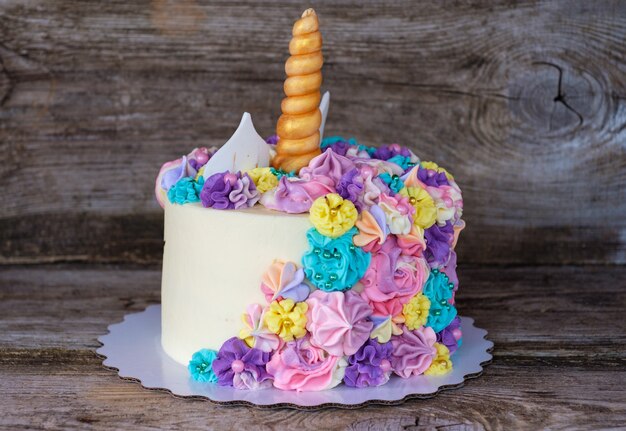 Hermoso pastel casero en forma de unicornio con flores de color crema sobre una mesa de madera