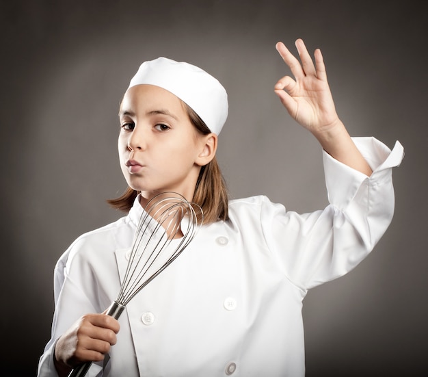 hermoso pequeño chef cocinando en la pared gris