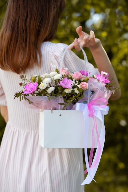 Un hermoso ramo de flores en una caja en manos de una hermosa chica que camina por la calle
