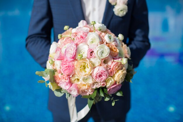 Hermoso ramo de flores frescas en manos del novio en la piscina del hotel.