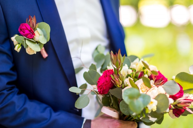 Hermoso ramo de flores mezcladas en manos de un novio en traje azul.