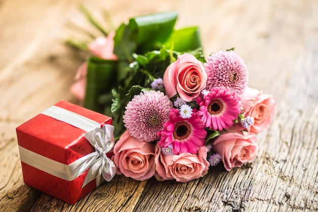 Hermoso ramo de flores con regalo rojo sobre mesa de madera.