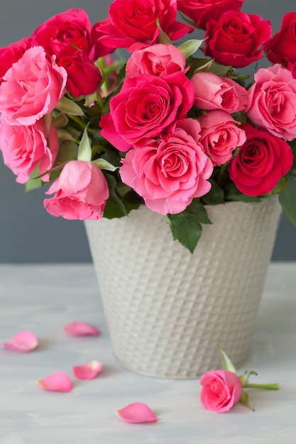 Hermoso ramo de flores rosas rojas en florero sobre gris