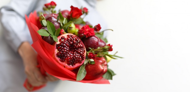 Hermoso ramo de frutas y rosas en manos de una mujer.