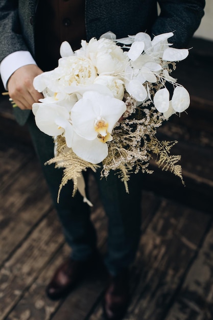 Hermoso ramo de novia de orquídeas blancas y peonías en manos del novio