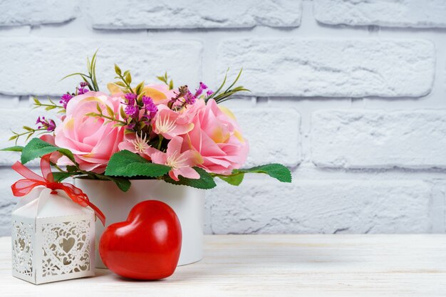 Hermoso ramo romántico de rosas rosadas con forma de corazón rojo y caja de regalo calada sobre fondo de pared de ladrillo blanco. Día de San Valentín, concepto de boda.