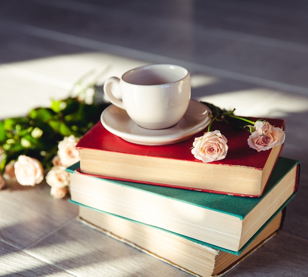 Hermoso ramo de rosas al sol en los libros con una taza