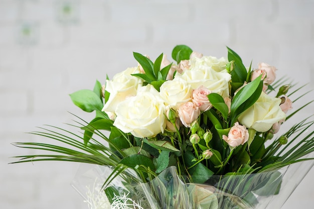 Hermoso ramo con rosas blancas fragantes frescas y hierba decorativa contra una pared blanca