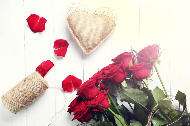 Foto hermoso ramo de rosas rojas y corazón de cilicio sobre fondo de madera