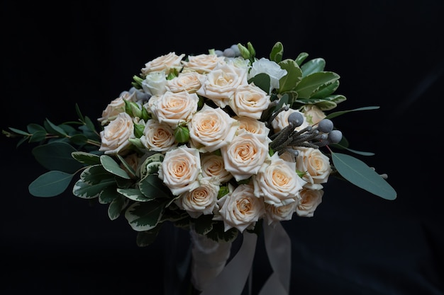 Hermoso ramo de rosas tupidas, eucaliptos, brunei, pittosporum y lisianthus en una pared negra.