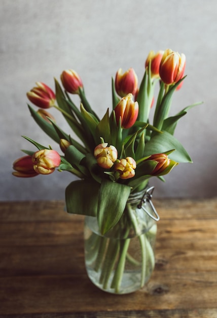 Hermoso ramo de tulipanes en un frasco de vidrio sobre una mesa de madera