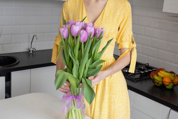 Hermoso ramo de tulipanes de primavera se encuentra sobre una mesa en la cocina Una mujer con un vestido amarillo