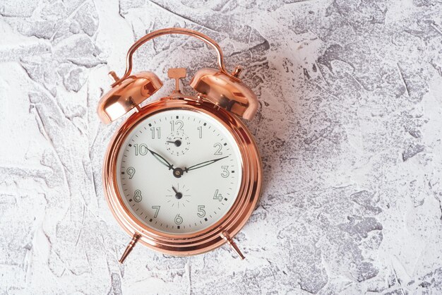 Hermoso reloj despertador vintage hecho de metal dorado sobre una superficie de textura blanca Buenos días Despertar Espacio de copia Primer reloj despertador mecánico vista superior