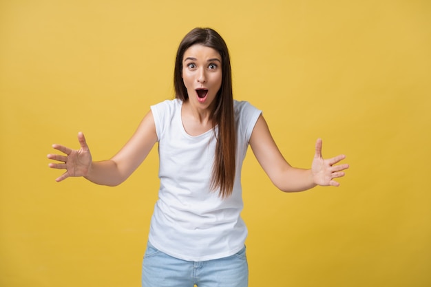 Hermoso retrato femenino de medio cuerpo aislado sobre fondo amarillo de estudio. La joven mujer sonriente y sorprendida emocional de pie y mirando a la cámara.Las emociones humanas, el concepto de expresión facial