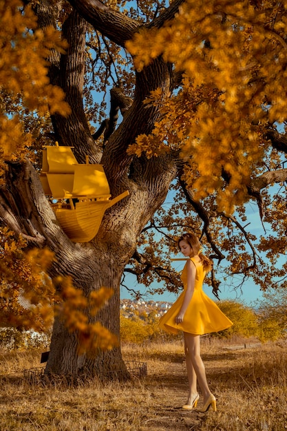 Hermoso retrato de mujer pelirroja con libro y barco cerca de roble en otoño