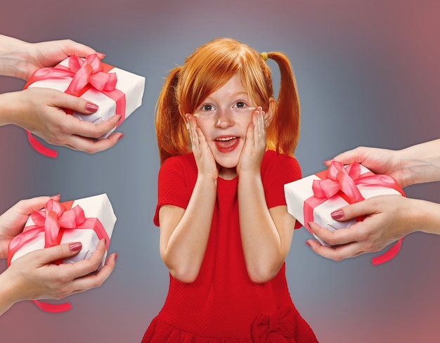 El hermoso retrato de una niña sorprendida con el pelo rojo en vestido rojo sobre azul con regalos