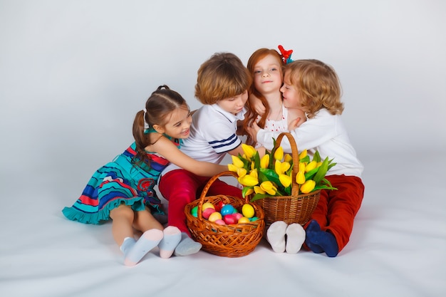 Hermoso retrato de niños que se sientan junto con una canasta de tulipanes y una canasta con huevos de Pascua. Momentos divertidos.