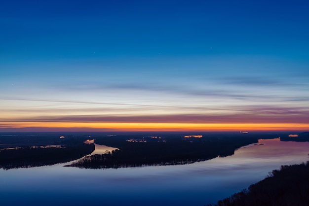 Hermoso río con isla grande con árboles bajo el cielo antes del amanecer.