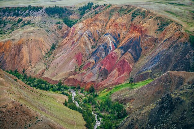 Hermoso río de montaña y árboles verdes en el valle entre colinas de arcilla multicolor. Paisaje escénico con arroyo de montaña en un colorido cañón y vívidas montañas multicolores. Pintoresco paisaje de montañas