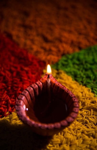 Hermoso saludo de Diwali con Diya o lámpara de aceite de arcilla encendida y dispuesta sobre Rangoli hecha por granos de arroz multicolores, enfoque selectivo