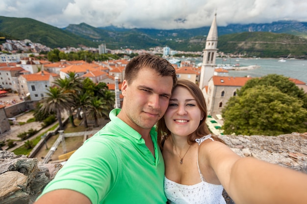 Hermoso selfie de joven pareja enamorada posando contra la ciudad vieja de Budva, Montenegro